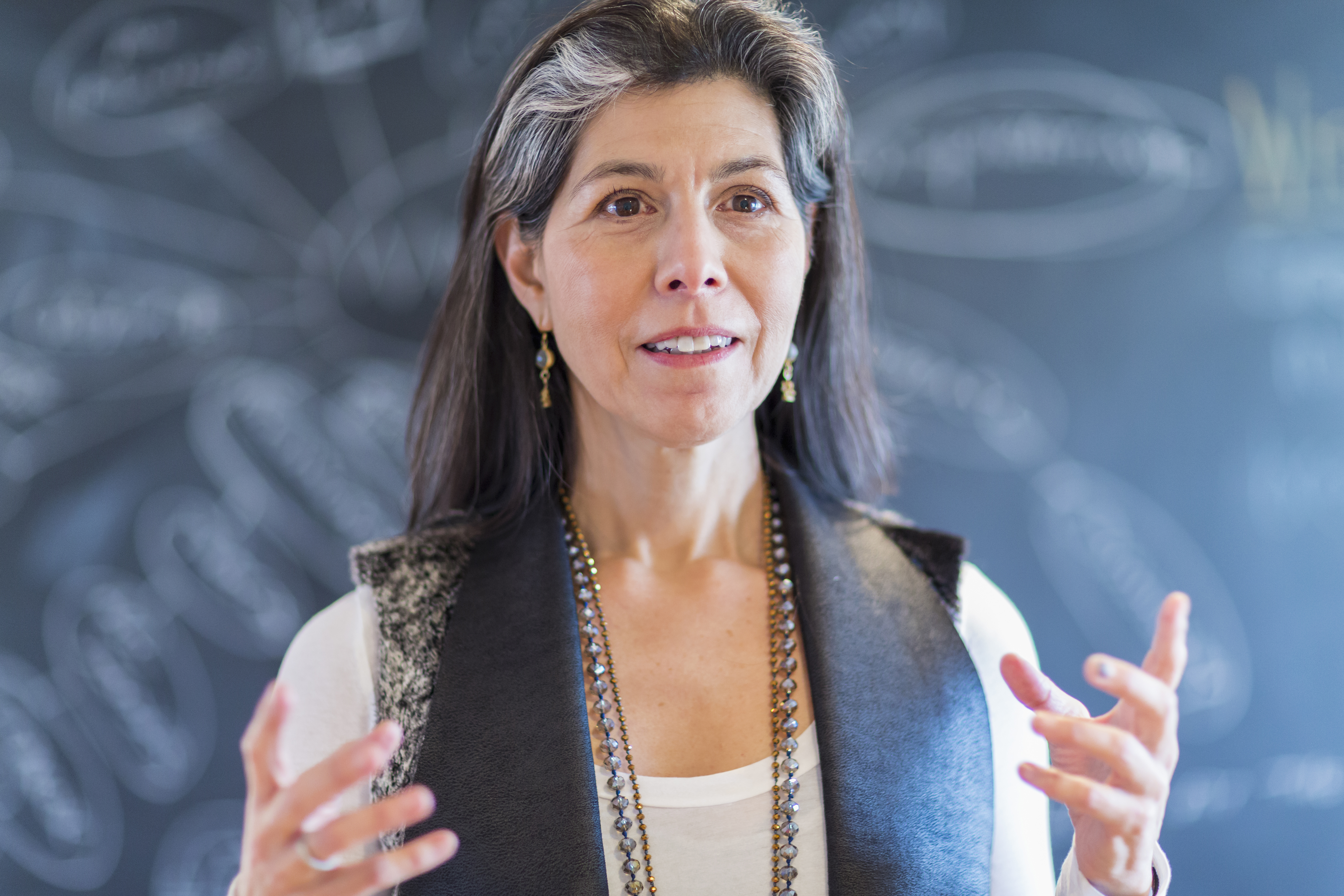 A woman talking in front of a chalkboard and expressing with her hands. 